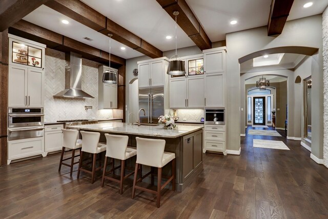 5111 Water Oak Cres, Fulshear, TX 77441 - kitchen with wall chimney range hood, arched walkways, a kitchen breakfast bar, stainless steel appliances, and tasteful backsplash