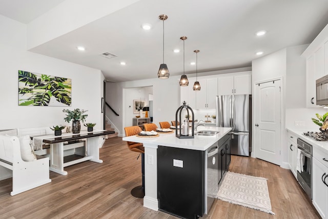 kitchen with light countertops, visible vents, light wood finished floors, a center island with sink, and appliances with stainless steel finishes