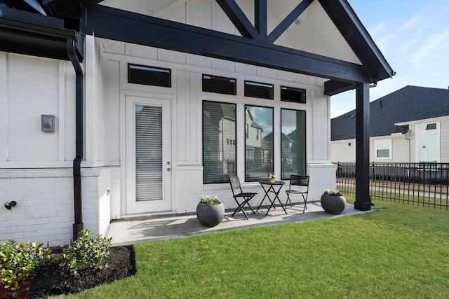 doorway to property featuring brick siding, fence, and a lawn