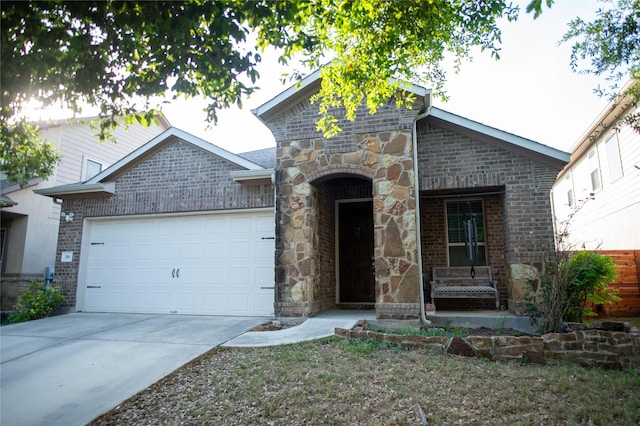 french country inspired facade featuring an attached garage, concrete driveway, brick siding, and stone siding