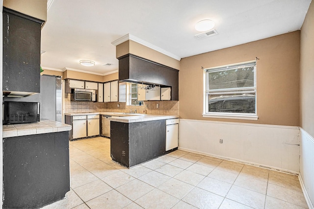 kitchen featuring a wainscoted wall, crown molding, a peninsula, stainless steel microwave, and visible vents