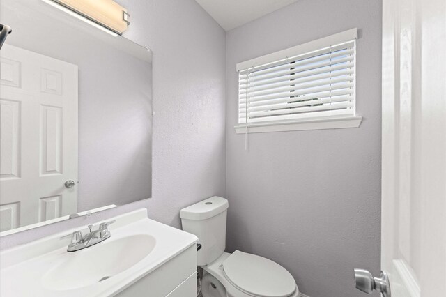 bathroom featuring a textured wall, toilet, and vanity