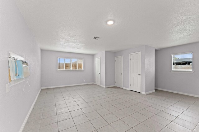 empty room with baseboards, a textured ceiling, a wealth of natural light, and visible vents