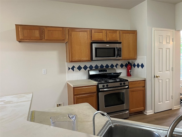 kitchen featuring tasteful backsplash, light countertops, brown cabinetry, wood finished floors, and stainless steel appliances