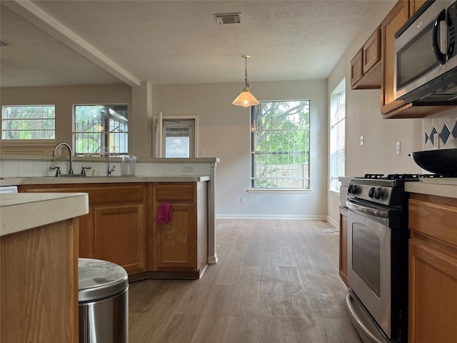 kitchen featuring brown cabinets, light countertops, appliances with stainless steel finishes, and light wood-style flooring
