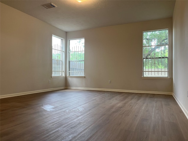 spare room featuring plenty of natural light, dark wood-style floors, baseboards, and visible vents