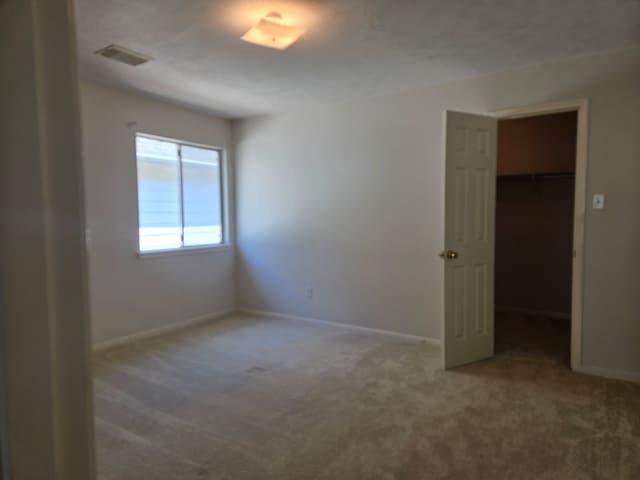 unfurnished bedroom featuring a walk in closet, baseboards, visible vents, and carpet floors