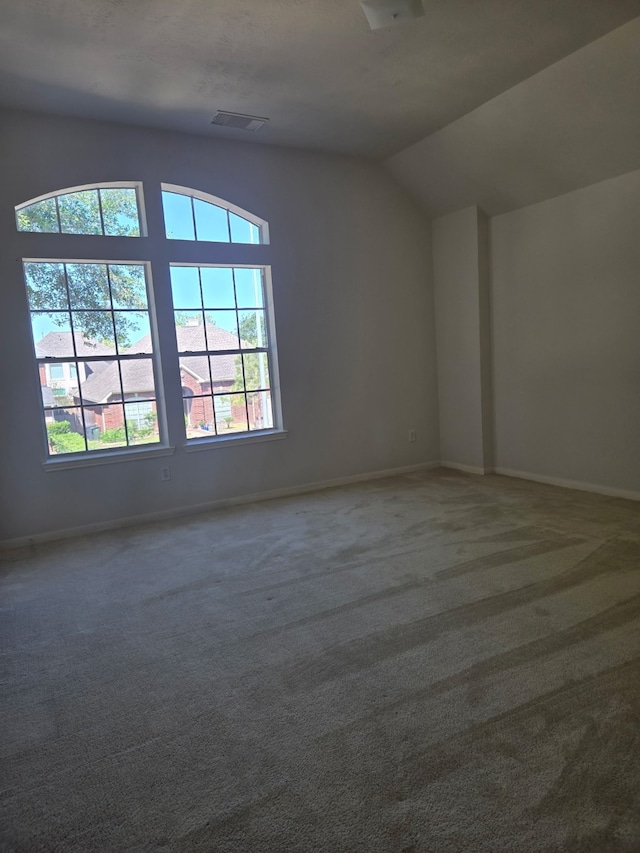 carpeted empty room with visible vents, baseboards, and vaulted ceiling