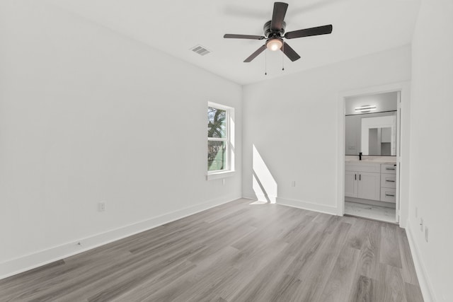 unfurnished bedroom featuring ensuite bathroom, light wood-style flooring, visible vents, baseboards, and ceiling fan