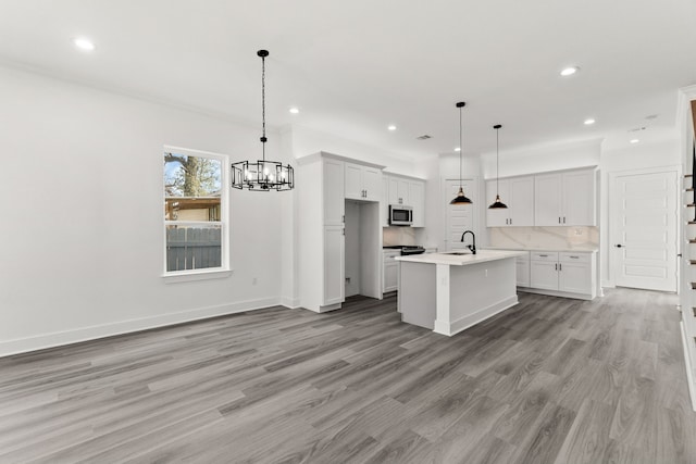 kitchen with an island with sink, a chandelier, light wood finished floors, stainless steel microwave, and recessed lighting