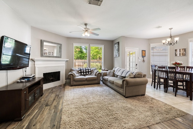 living area featuring a fireplace, visible vents, a healthy amount of sunlight, and ceiling fan with notable chandelier