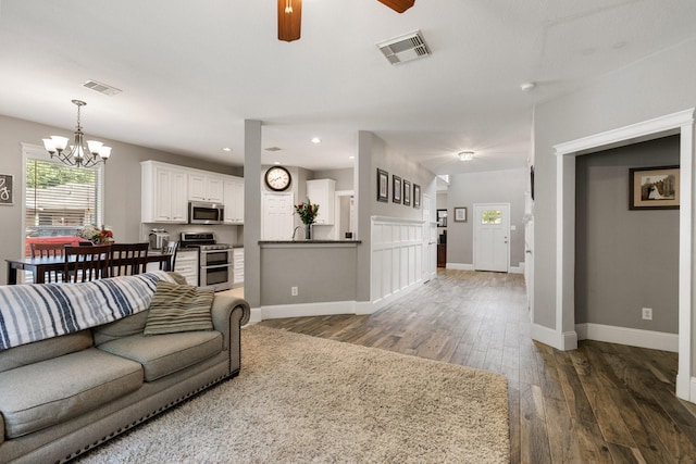 living area with ceiling fan with notable chandelier, baseboards, hardwood / wood-style flooring, and visible vents