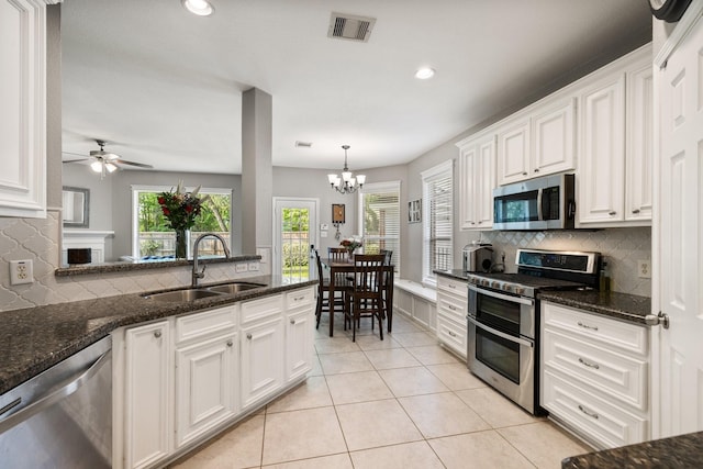 kitchen featuring white cabinets, a sink, tasteful backsplash, ceiling fan with notable chandelier, and appliances with stainless steel finishes