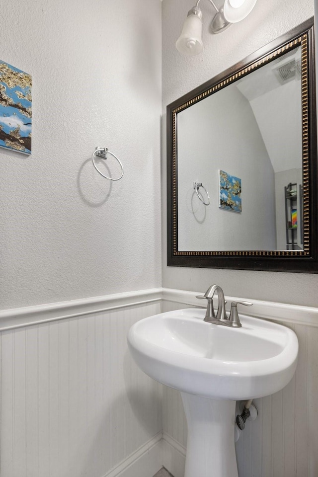 bathroom with a textured wall, a wainscoted wall, visible vents, and vaulted ceiling
