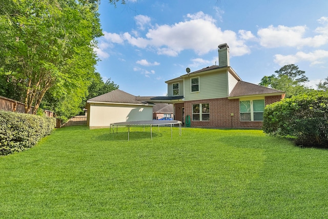back of property with brick siding, fence, a yard, and a trampoline