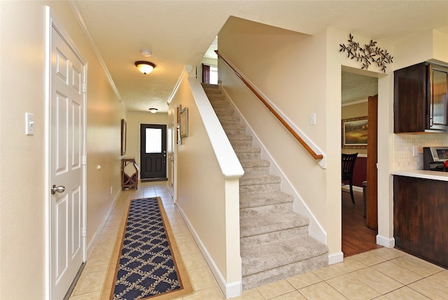 interior space with light tile patterned flooring, baseboards, stairs, and ornamental molding