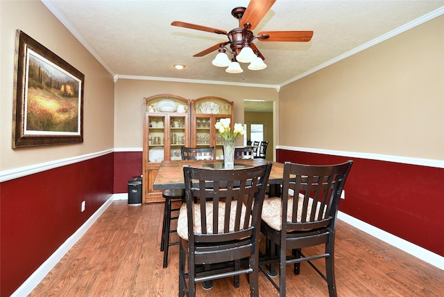 dining space featuring crown molding, a ceiling fan, wood finished floors, a textured ceiling, and baseboards