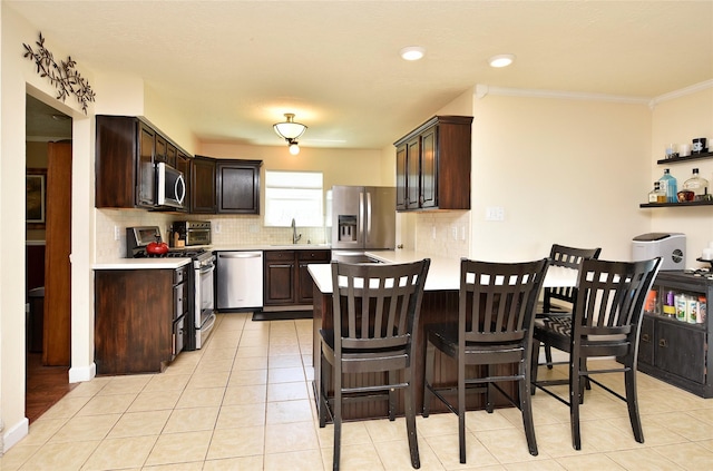 kitchen with stainless steel appliances, light countertops, a sink, dark brown cabinetry, and tasteful backsplash
