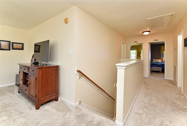 corridor with attic access, baseboards, light carpet, and an upstairs landing