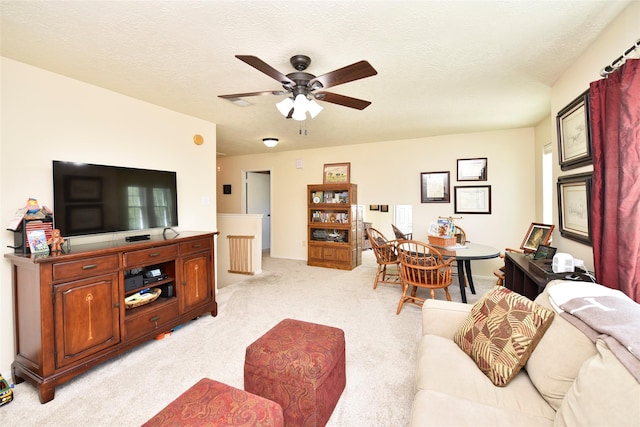 living room featuring light colored carpet, ceiling fan, baseboards, and a textured ceiling