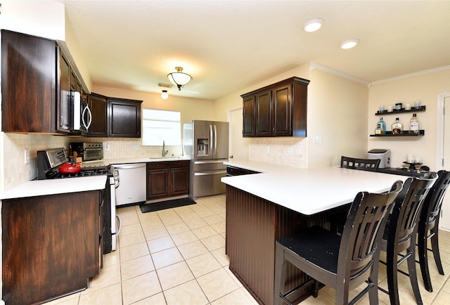 kitchen with stainless steel appliances, dark brown cabinetry, decorative backsplash, a peninsula, and a breakfast bar area