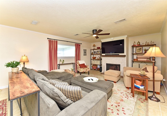 living area featuring a tiled fireplace, visible vents, a ceiling fan, tile patterned flooring, and crown molding