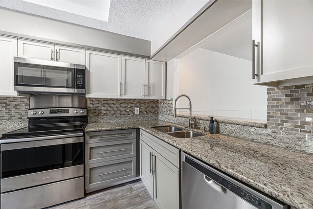3226 Poe Dr, Montgomery, TX 77356 - kitchen featuring light stone countertops, tasteful backsplash, white cabinetry, appliances with stainless steel finishes, and a sink