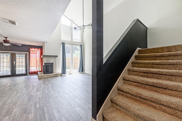 3226 Poe Dr, Montgomery, TX 77356 - stairway featuring visible vents, a fireplace with raised hearth, ceiling fan, a towering ceiling, and wood finished floors