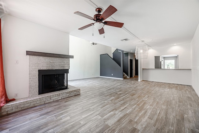 3226 Poe Dr, Montgomery, TX 77356 - unfurnished living room with ceiling fan, visible vents, wood finished floors, a brick fireplace, and stairs