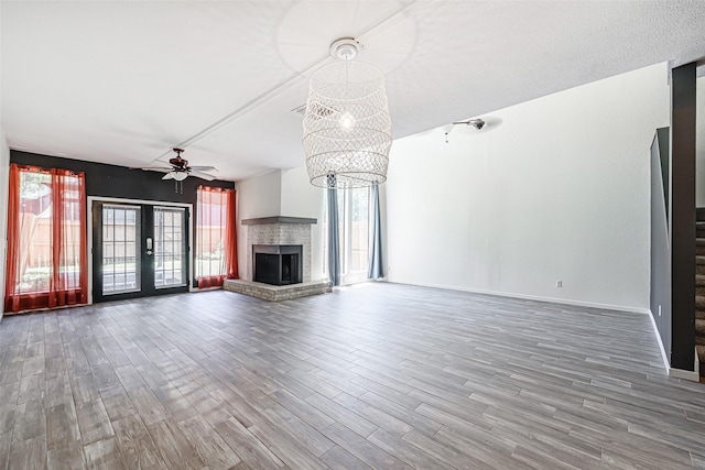 3226 Poe Dr, Montgomery, TX 77356 - unfurnished living room featuring a fireplace, baseboards, wood finished floors, and ceiling fan with notable chandelier