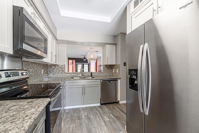 3226 Poe Dr, Montgomery, TX 77356 - kitchen with a raised ceiling, a sink, appliances with stainless steel finishes, light wood-style floors, and decorative backsplash