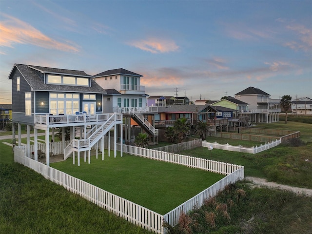 17431 Bristow Dr, Galveston, TX 77554 - back of property at dusk with stairway, a wooden deck, a fenced backyard, a shingled roof, and a yard