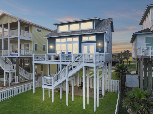 17431 Bristow Dr, Galveston, TX 77554 - back of house at dusk featuring fence, a patio, stairs, roof with shingles, and a yard