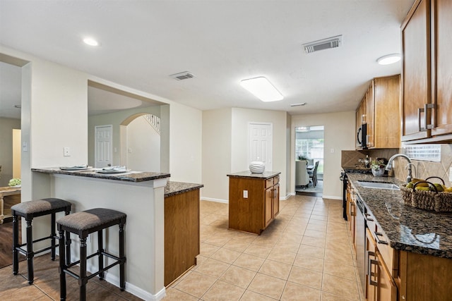 7107 Grant Dr, Magnolia, TX 77354 - kitchen with a sink, brown cabinets, a breakfast bar, dark stone counters, and a kitchen island