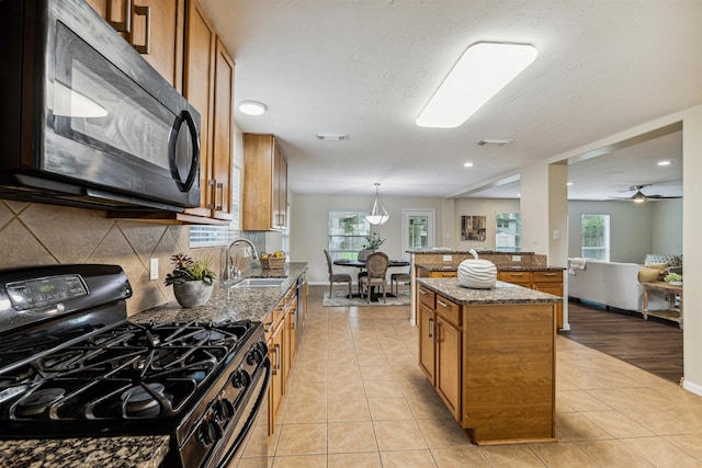 7107 Grant Dr, Magnolia, TX 77354 - kitchen featuring range with gas stovetop, black microwave, brown cabinetry, a sink, and tasteful backsplash