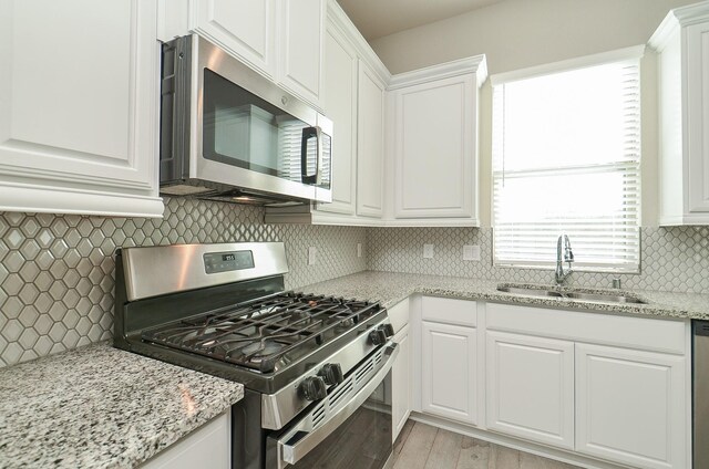 5203 Prairie Terrace Ln, Fulshear, TX 77441 - kitchen featuring light stone counters, a sink, appliances with stainless steel finishes, white cabinets, and decorative backsplash