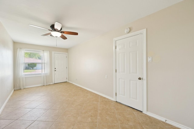 empty room with a ceiling fan, light tile patterned floors, and baseboards