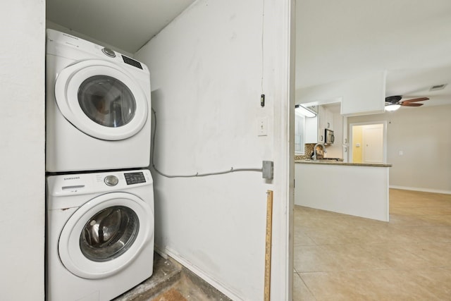laundry room featuring baseboards, stacked washing maching and dryer, a sink, ceiling fan, and laundry area