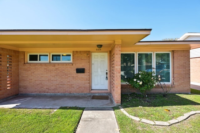 entrance to property featuring brick siding and a yard