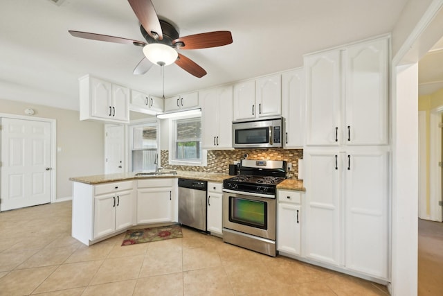 kitchen with a peninsula, stainless steel appliances, white cabinetry, a sink, and backsplash