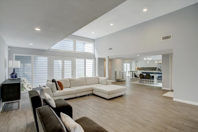 living area featuring a towering ceiling, visible vents, light wood-type flooring, baseboards, and a chandelier