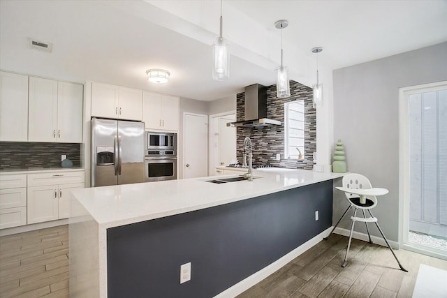 kitchen with stainless steel appliances, light countertops, wall chimney range hood, visible vents, and tasteful backsplash