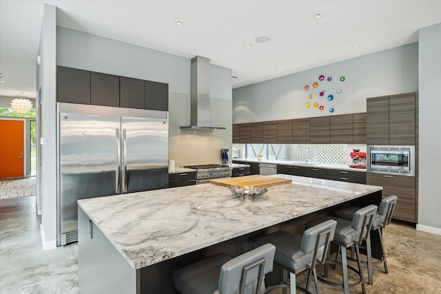 kitchen with wall chimney exhaust hood, modern cabinets, a center island, decorative backsplash, and built in appliances