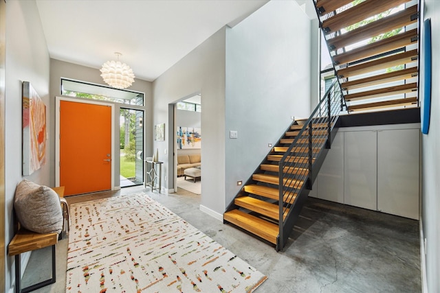 foyer featuring a chandelier, concrete flooring, baseboards, and stairway