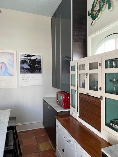 kitchen with dark tile patterned flooring, baseboards, white cabinetry, and glass insert cabinets