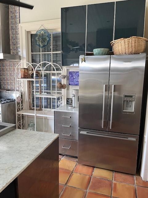 kitchen with stainless steel fridge with ice dispenser, ventilation hood, light countertops, and light tile patterned flooring