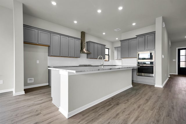 2904 Apple Rose, Katy, TX 77493 - kitchen with wall chimney range hood, oven, a kitchen island with sink, light wood-type flooring, and built in microwave