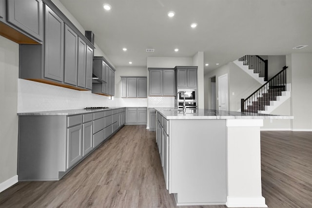 2904 Apple Rose, Katy, TX 77493 - kitchen with backsplash, light wood finished floors, a kitchen island with sink, and gray cabinetry