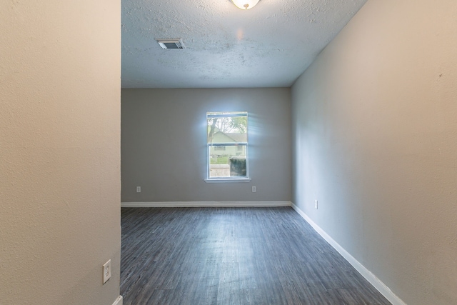 empty room featuring baseboards, dark wood-style flooring, a textured ceiling, and visible vents