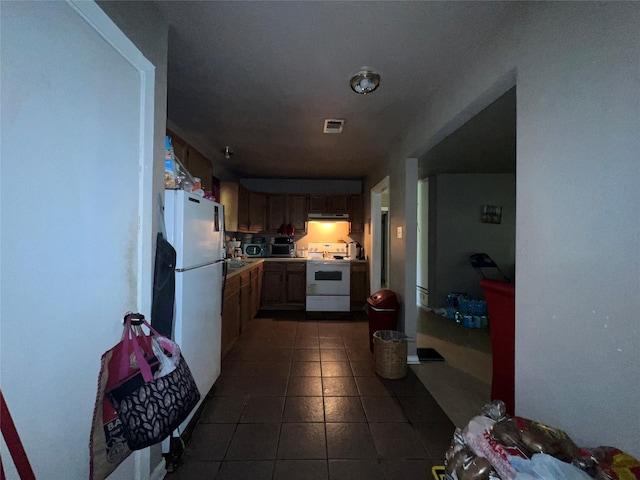 kitchen with light countertops, white appliances, under cabinet range hood, dark tile patterned flooring, and visible vents